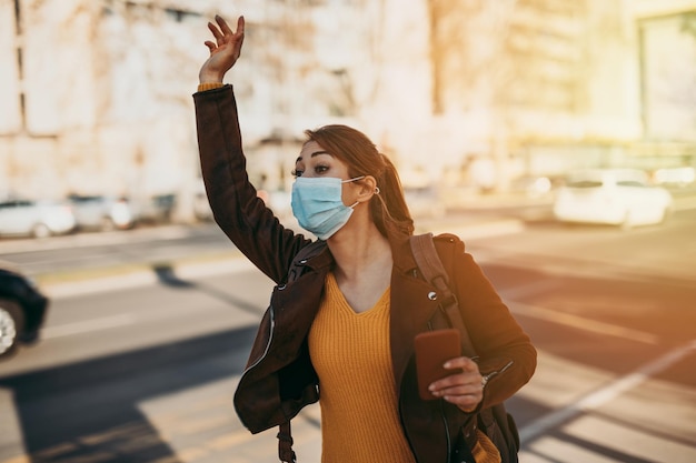 Elegant business woman with protective mask standing alone on empty street and waiting for bus or taxi transport. Corona virus or Covid-19 lifestyle concept.