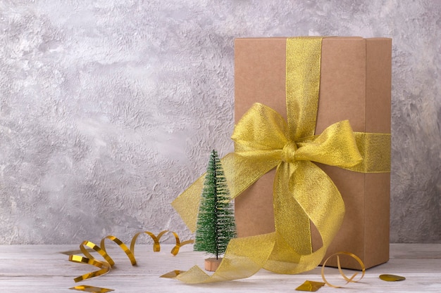 Elegant cardboard gift box with golden ribbon near miniature christmas tree model