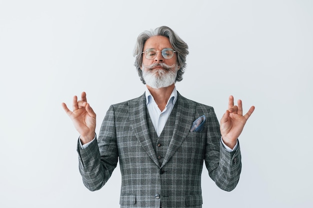 In elegant clothes Standing against white wall Senior stylish modern man with grey hair and beard indoors