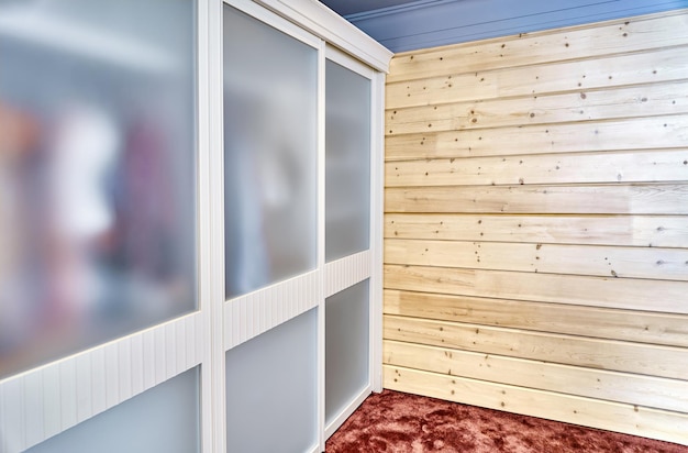 Elegant contemporary wardrobe with clothes and matte glass on sliding door stands near wooden wall