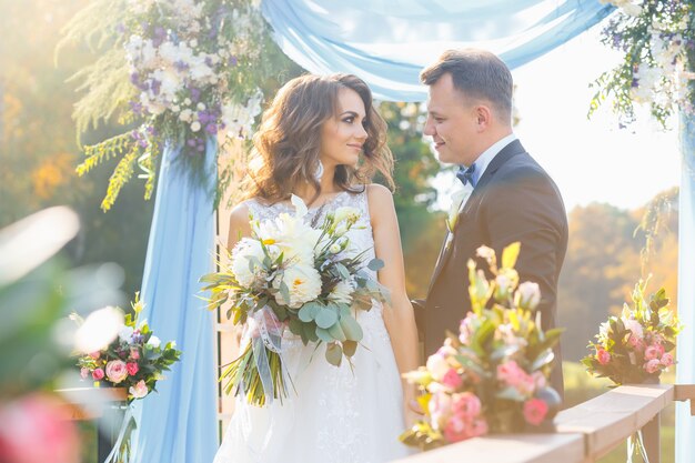 Elegant curly bride and happy groom outdoors on the background the lake. Creative stylish wedding ceremony