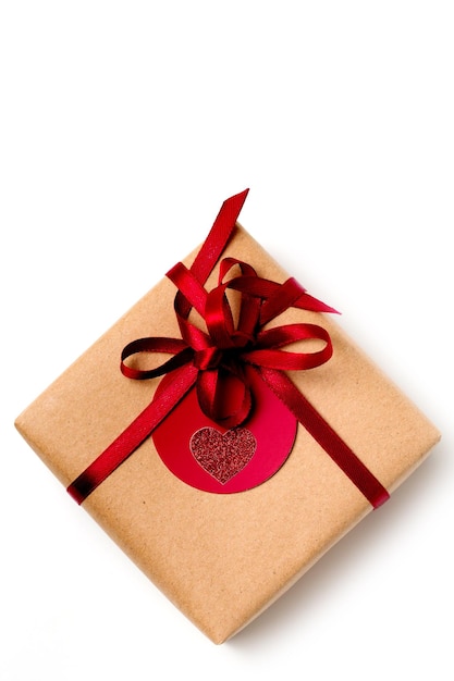 Elegant design of present gift box wrapped in brown craft paper with red ribbon, top view on white background