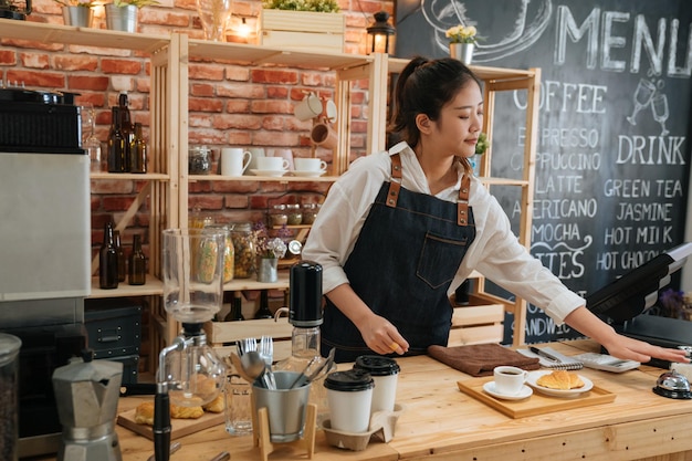 elegant female barista preparing customer meal in bar counter at modern cafe. young girl coffeehouse staff ready for hot coffee and croissant pressing ring. worker ringing service bell calling waiter