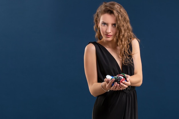 Photo elegant female casino player holding a handful of chips on dark blue background. copy space