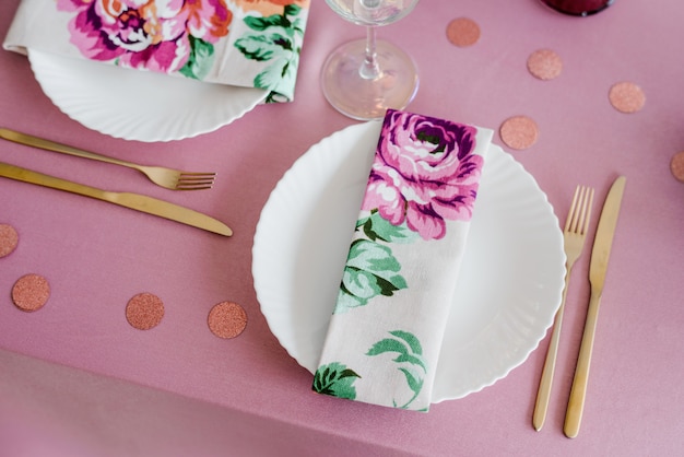 Elegant festive table setting in pink tones with floral textile napkins, golden fork and knife, confetti. Wedding, birthday, baby shower, girl party decoration.