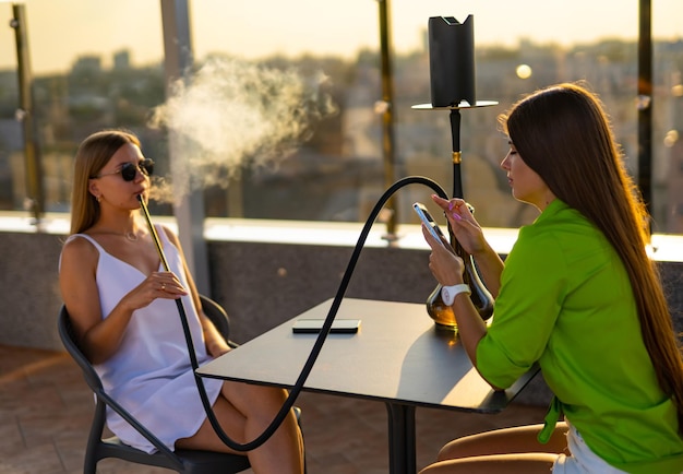 Elegant girls in bar smoking Young ladies relaxing with hookah