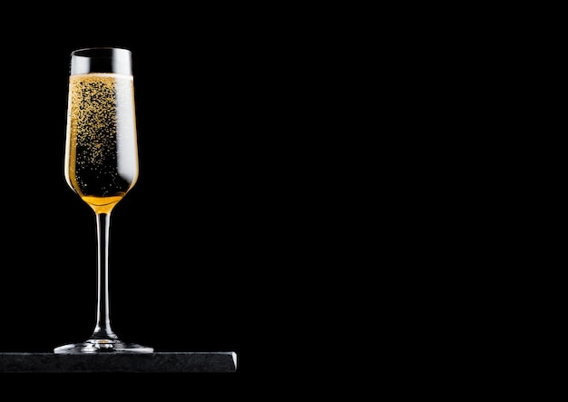 Elegant glass of yellow champagne with bubbles on black marble board on black background