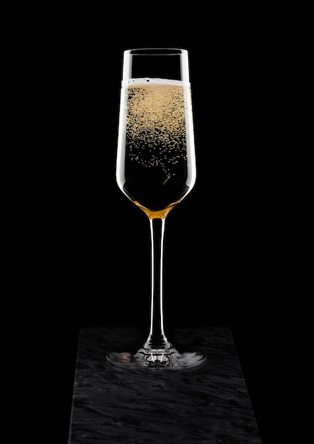 Elegant glass of yellow champagne with bubbles on black marble board on black