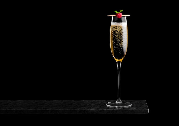 Elegant glass of yellow champagne with rasspbery on stick on black marble board on black background