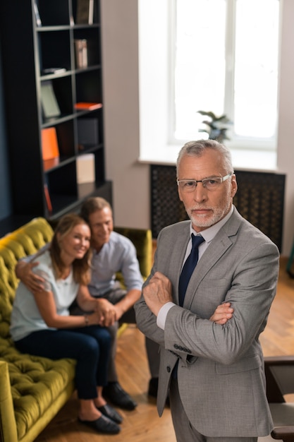 Elegant good-looking psychoanalyst standing next to a smiling married couple during the therapy session in his office