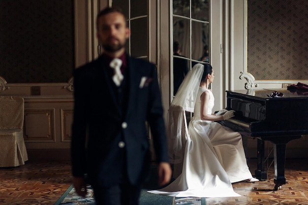 Elegant gorgeous bride playing the fortepiano and stylish handsome groom posing in rich old room sensual look unusual luxury wedding in retro style