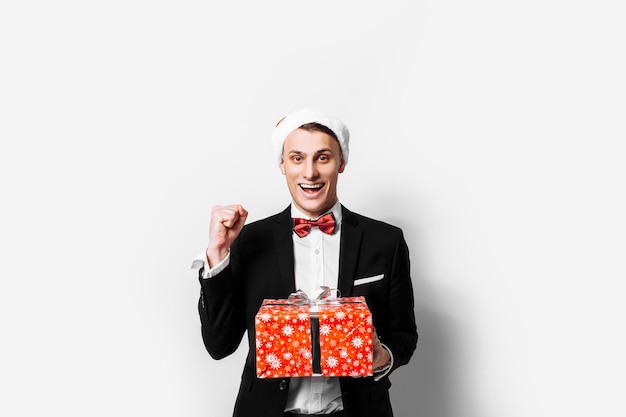 Elegant guy in the hat of Santa Claus with a Christmas gift in his hands