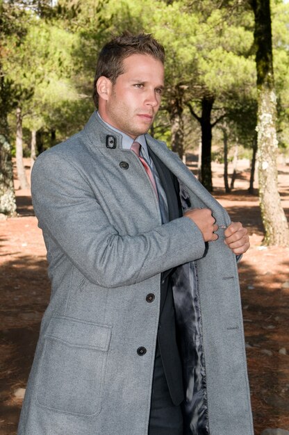 Photo elegant man in his coat in the middle of the field among the pines