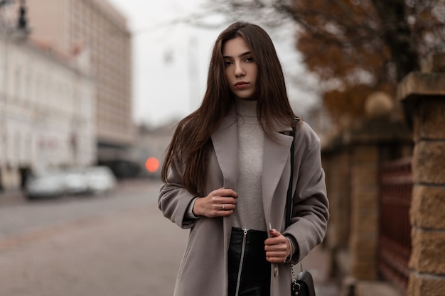 Elegant model with brown long hair in a stylish coat posing in the city on an autumn day