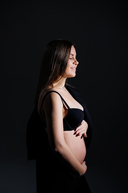 Elegant pregnant woman Beautiful pregnant girl with long hair in black suit on gray background concept of happy pregnancy and family