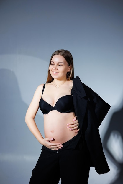 Elegant pregnant woman Beautiful pregnant girl with long hair in black suit on gray background concept of happy pregnancy and family