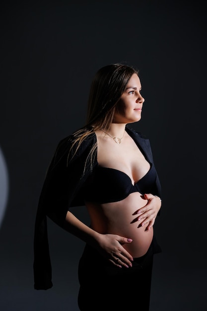 Elegant pregnant woman Beautiful pregnant girl with long hair in black suit on gray background concept of happy pregnancy and family