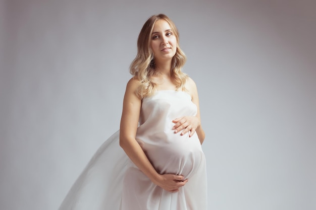 Elegant pregnant young woman standing wearing light fabric Pregnancy fantasy and fairy tale concept