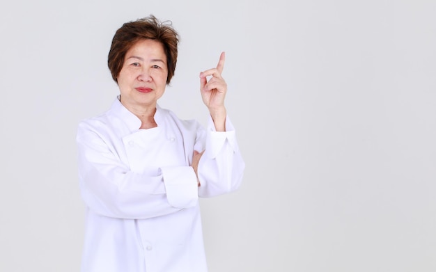 Elegant senior woman as professional chef confidently standing with arm crossed and wooden spoon and fork in restaurant kitchen. Elderly aunt expert in cooking for healthy cuisine of retired person.