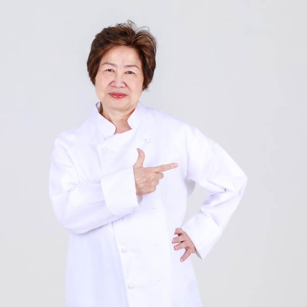 Elegant senior woman as professional chef confidently standing with arm crossed and wooden spoon and fork in restaurant kitchen. Elderly aunt expert in cooking for healthy cuisine of retired person.