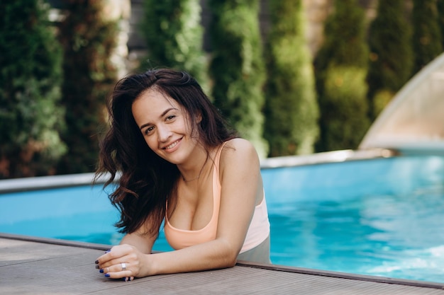 Elegant sexy woman in luxury bikini on the suntanned slim and shapely body is posing near the swimming pool Sunbathing By Swimming Pool On Travel Beauty Wellness Lifestyle Image