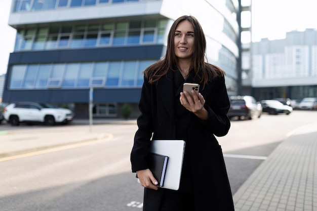 Elegant solid caucasian businesswoman with laptop and mobile phone outside