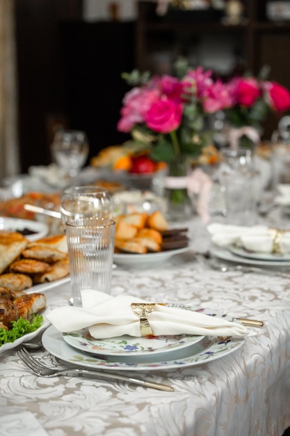 Elegant table setting with pink roses plates silverware crystal glasses on a patterned tablecloth