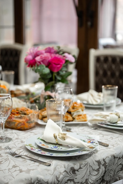 Elegant table setting with pink roses plates silverware crystal glasses on a patterned tablecloth