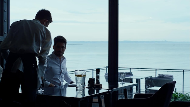 Elegant waiter serving successful businessman customer in seascape restaurant