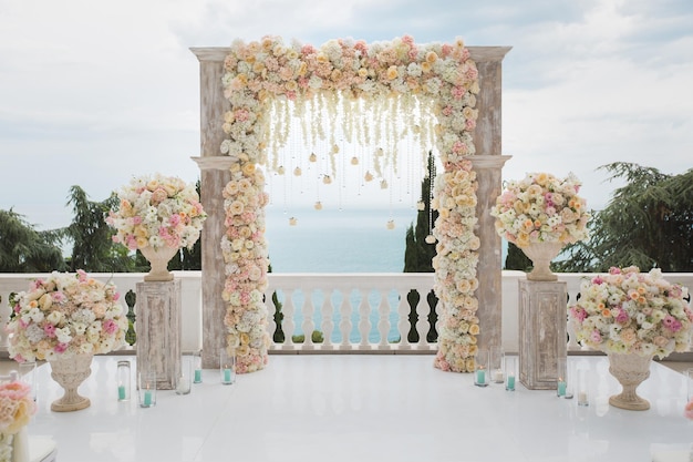 Elegant wedding arch with fresh flowers vases on background of ocean and blue sky