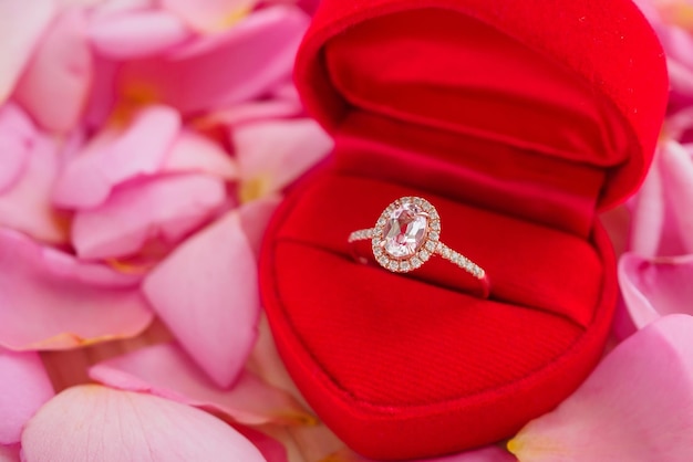 Elegant wedding diamond ring in red heart jewelry box on beautiful pink rose petal background