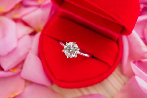 Elegant wedding diamond ring in red heart jewelry box on beautiful pink rose petal background