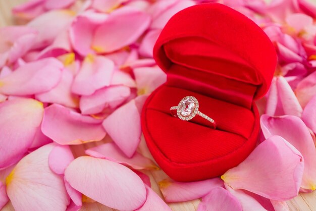 Elegant wedding diamond ring in red heart jewelry box on beautiful pink rose petal background