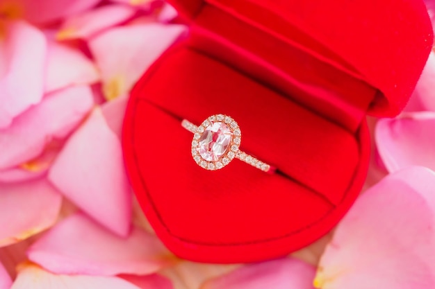 Elegant wedding diamond ring in red heart jewelry box on beautiful pink rose petal background