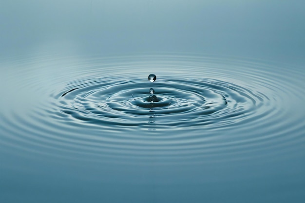 Elegant Within the center of an empty light blue canvas is a single raindrop creating ripples that