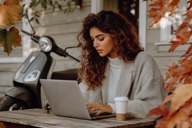 Photo an elegant woman in an autumn park works at her laptop while sitting on a chair near a cafe