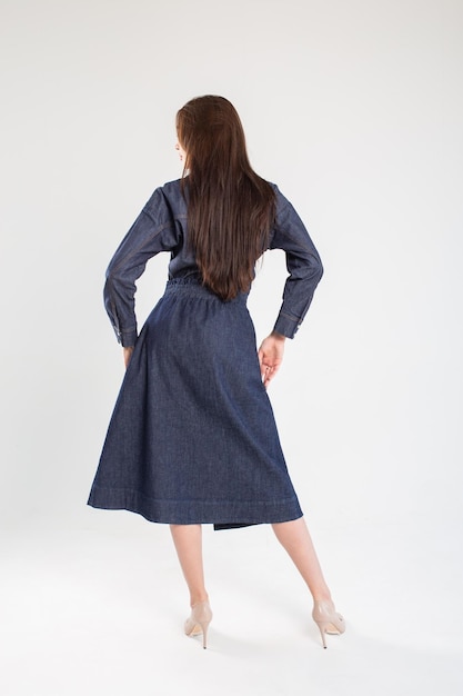 Elegant woman in a blue denim dress posing on a white background