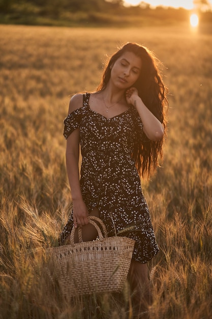 Elegant Woman In A Dress With Basket In The Wheat Field at sunset.