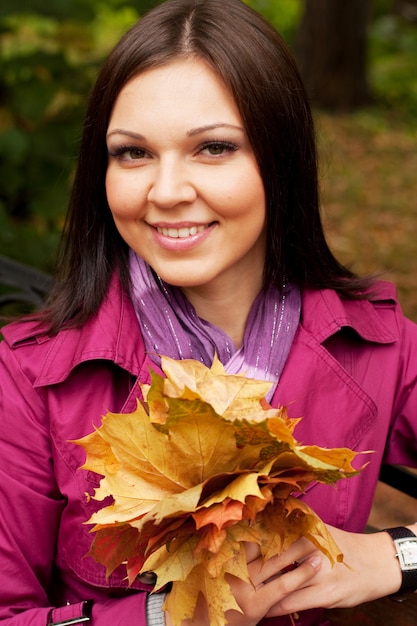 Elegant woman with autumn leaves sitting on bench