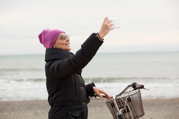 Elegant woman with bicycle and using a cellphone. Near the sea, space for text