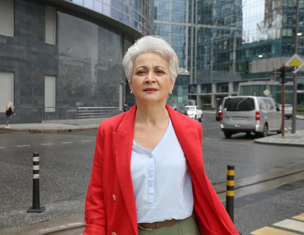 an elegant woman with gray hair in a red jacket on a city street