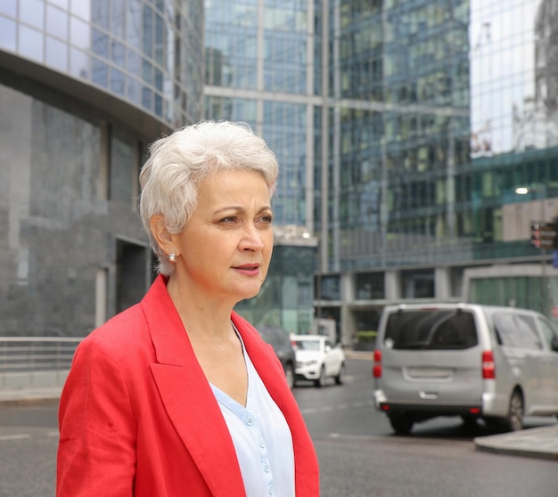 an elegant woman with gray hair in a red jacket on a city street