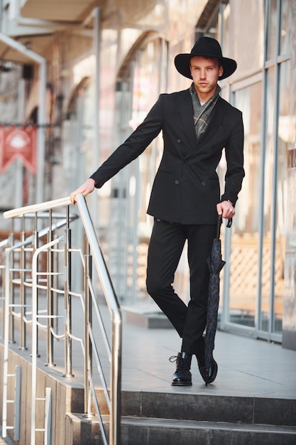 Elegant young man in black hat and with umbrella outdoors in the city