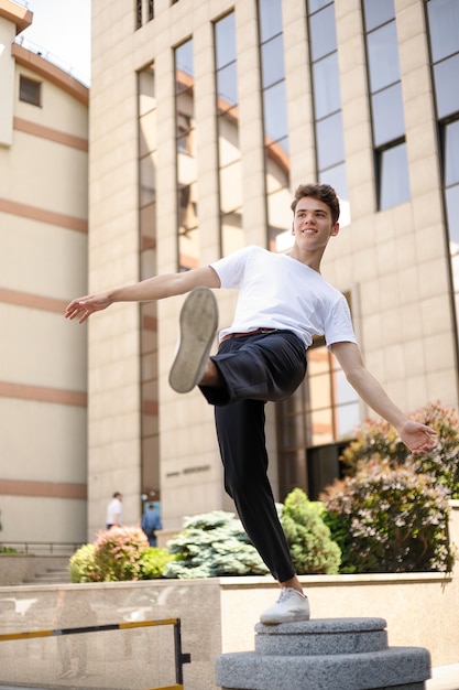 Elegant young man in a fashionable black shirt in a white stylish t-shirt in black pants with a trendy hairstyle rests near a modern business center. Attractive guy in the street on a summer day.