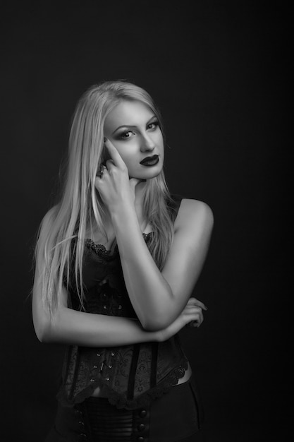 Elegant young model with bright makeup and long blond hair wears corset with lace. Black and white studio shot