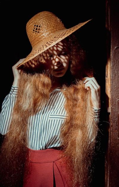 Elegant young red haired model with long wavy hair in straw hat