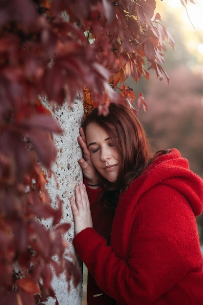 Elegant young woman in a burgundy casual coat in autumn Cute model walks in the park in golden autumn through colorful trees and fallen leaves Autumn walk colorful nature