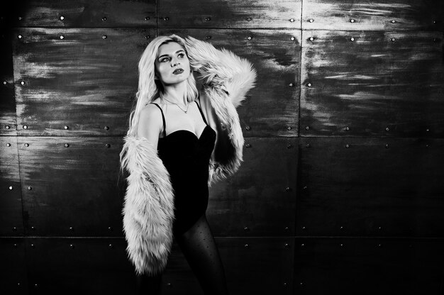 Elegante blonde girl wear on fur coat and combi dress posed against steel wall on studio.