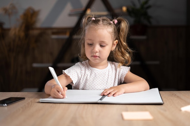 Elementary school child studies remotely at home doing homework in a notebook sitting in the room Prescooler learns to write with a pen Children and distance education Smart pupil