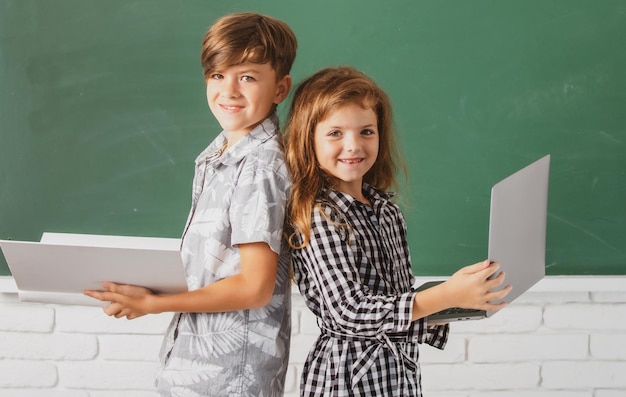 Elementary school kids portrait of children boy and girl with laptop computer and book at school kid